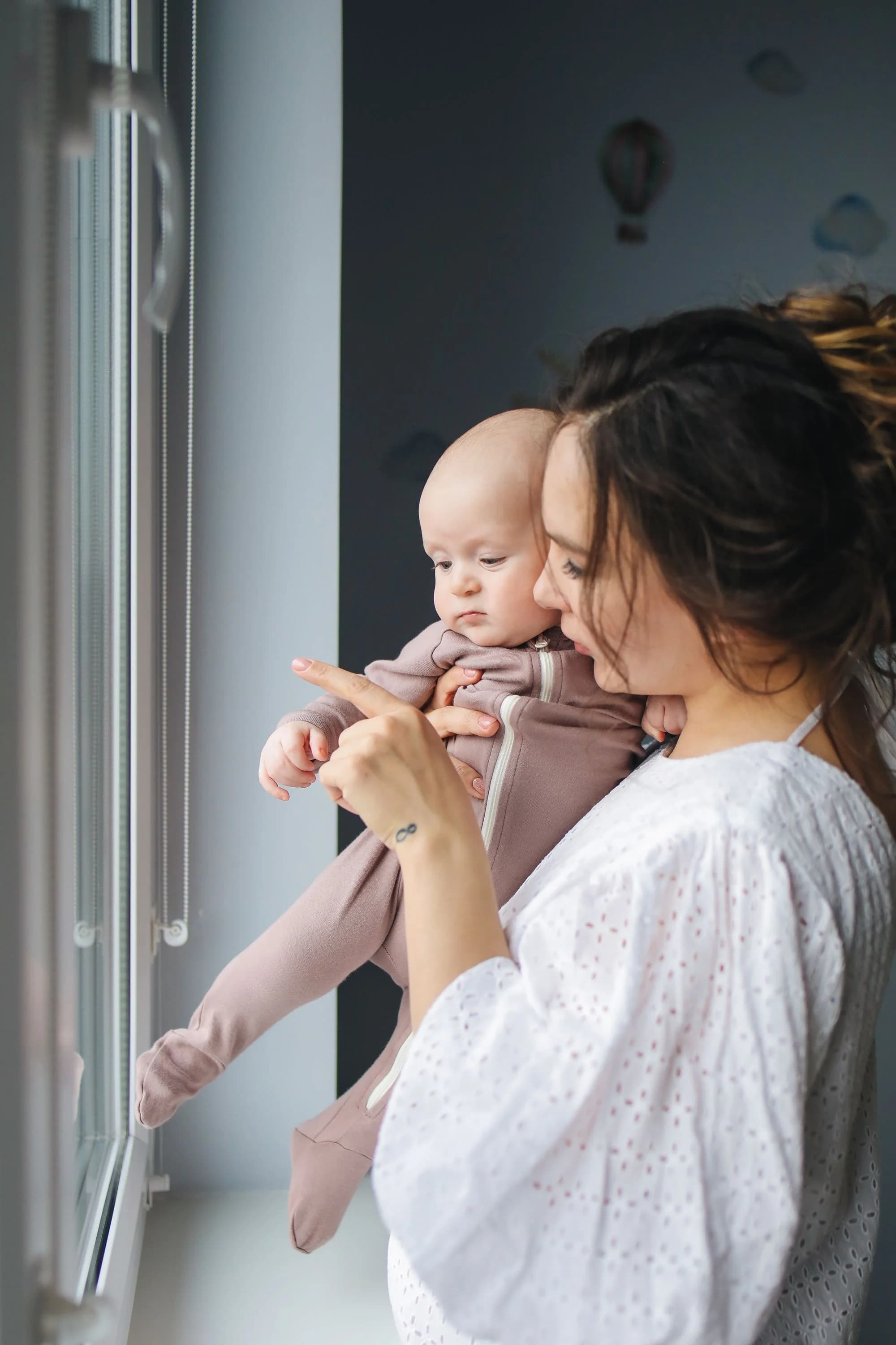 A mother holding her baby and pointing out the window